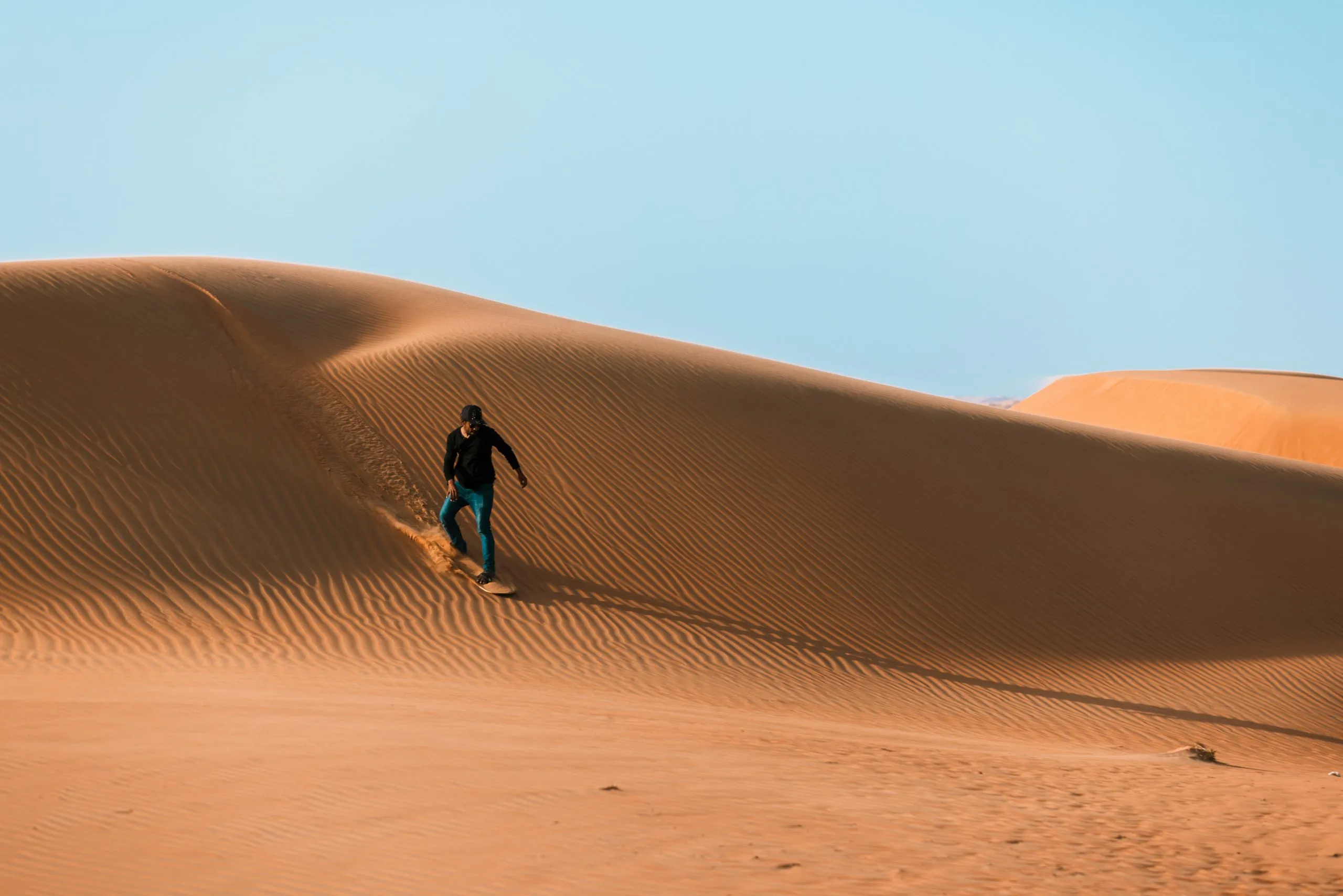 High quality stock photo of a man sliding down with a sand board in a dune in the Sultanate of Oman.