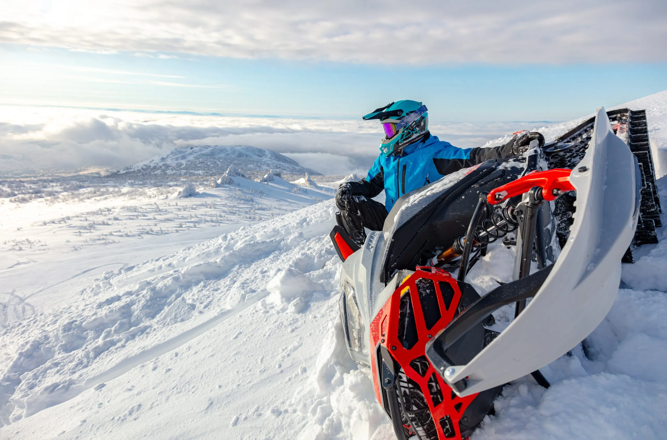 a snowmobiler is resting on top of a mountain, tipping the snowmobile on its side. snowmobile close-up with a sitting rider over the valley